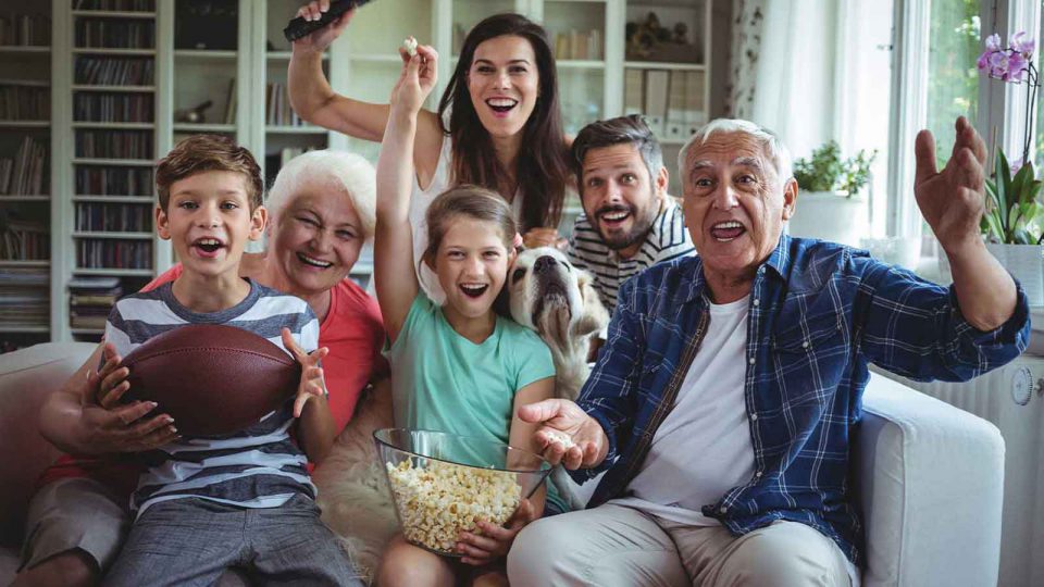 Famielie mit Oma und Opa und Hund schauen gemeinsam gespannt und fröhlich Fernsehen