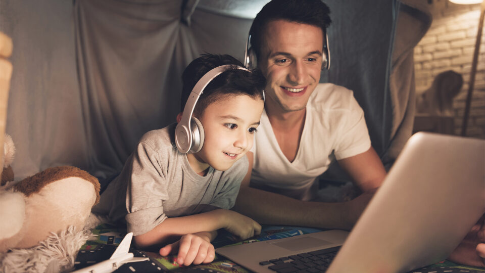 Vater und Sohn informieren sich in kuscheliger Atmosphäre mit dem Laptop über Glasfaser