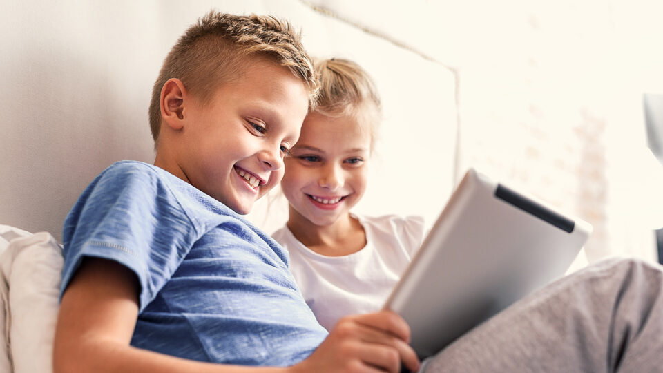 Geschwisterkinder surfen mit einem Tablet im Internet und haben viel Spaß dabei
