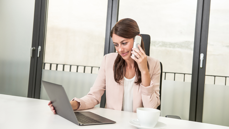 Frau sitzt am Laptop und telefoniert am Arbeitsplatz